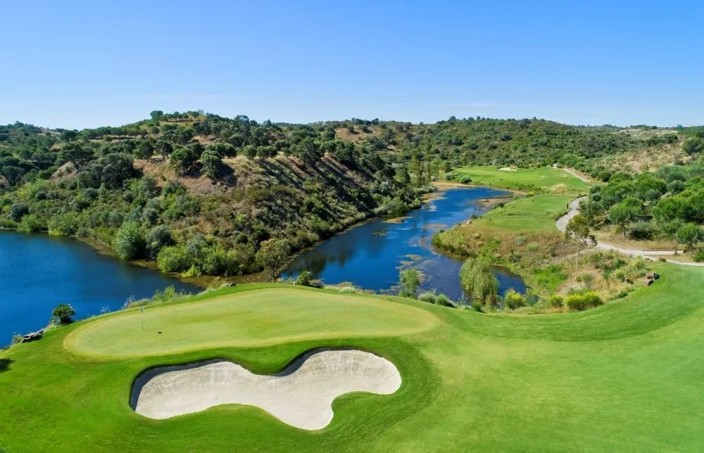 Monte Rei North Course green and bunker beside a winding lake · On-site golf